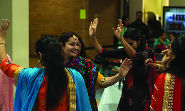 East Indian girls, dressed in colourful embroidered saris, dancing with hands in the air. 