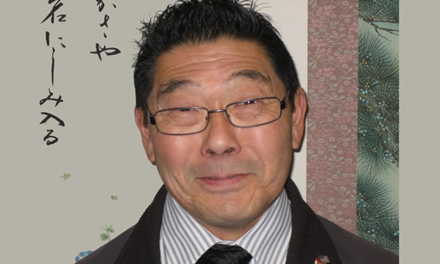 Ron Toyota wears glasses and a suit. He has black hair.