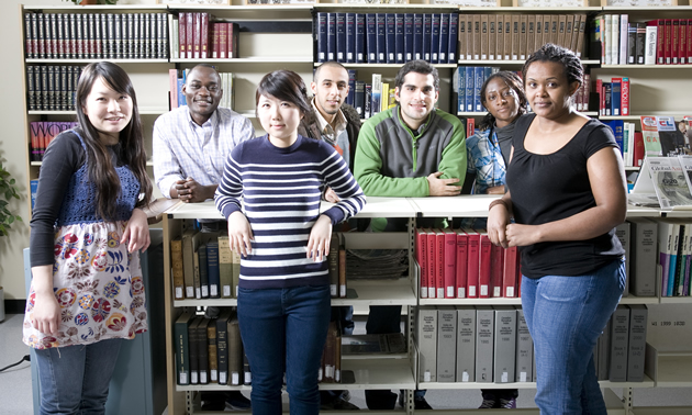 Seven young people of different races stand together in a library-like setting