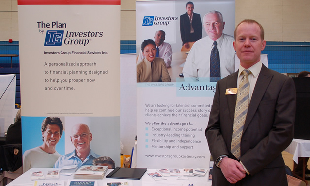 A representative in suit and tie smiles in front of boards explaining the advantages of employment at Investors Group.
