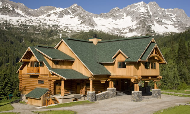 A large lodge with a green roof against a backdrop of mountains.