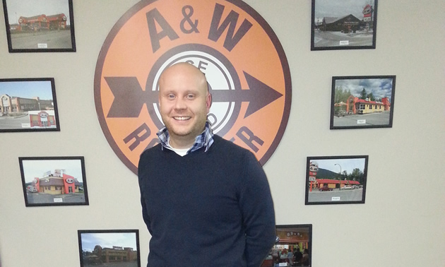 Close-up of a young, bald man in front of an A&W root beer sign.