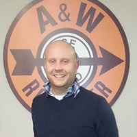 Close-up of a young, bald man in front of an A&W root beer sign.