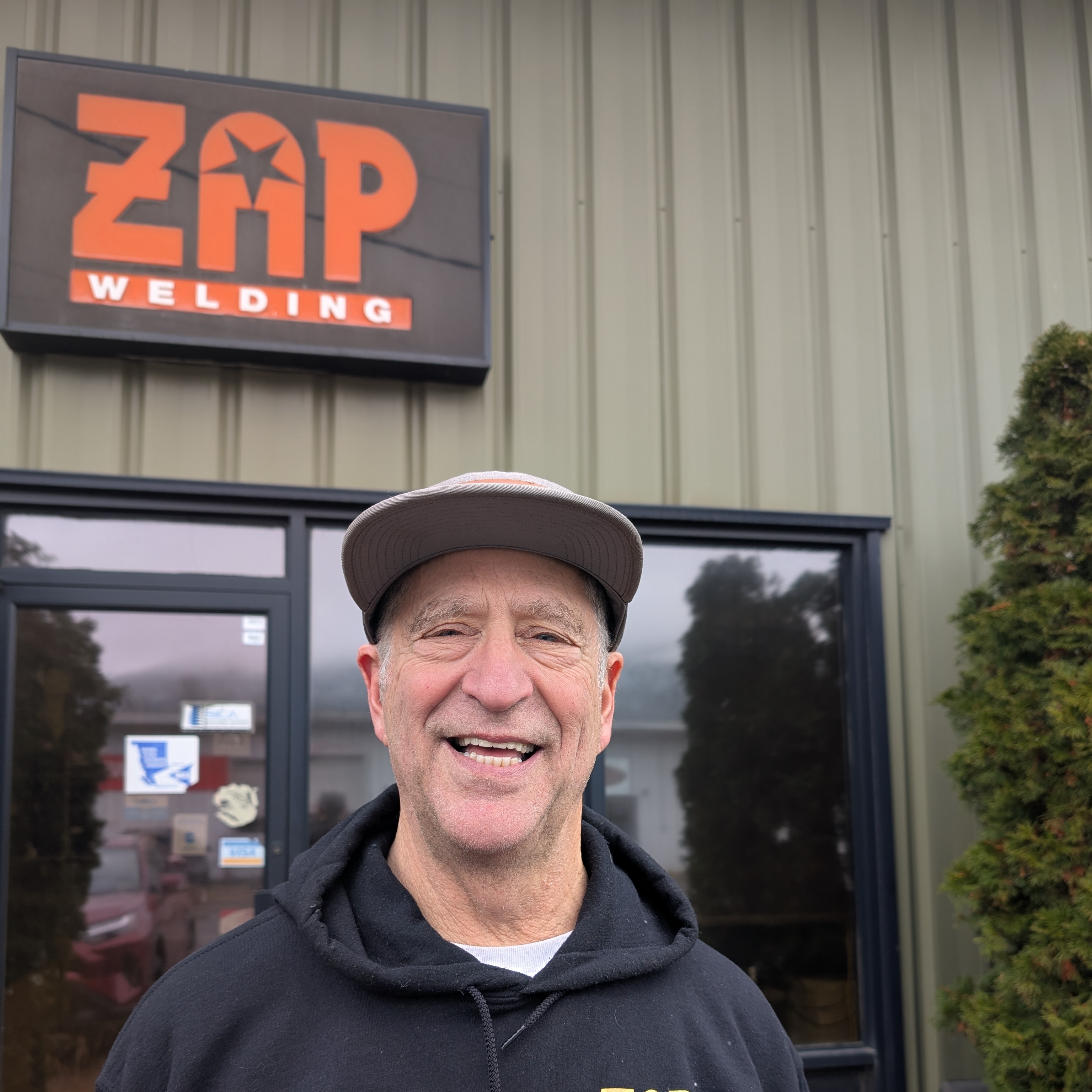 Owner of Zap, Jeff standing outside the Zap building and sign, wearing a baseball cap