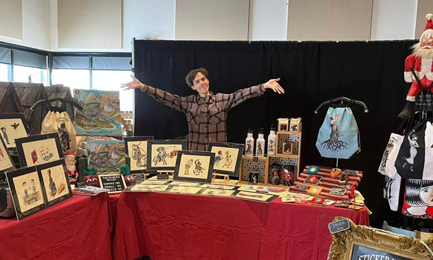 Japhy Hunt—hands in the air—standing at market display table with his work. 