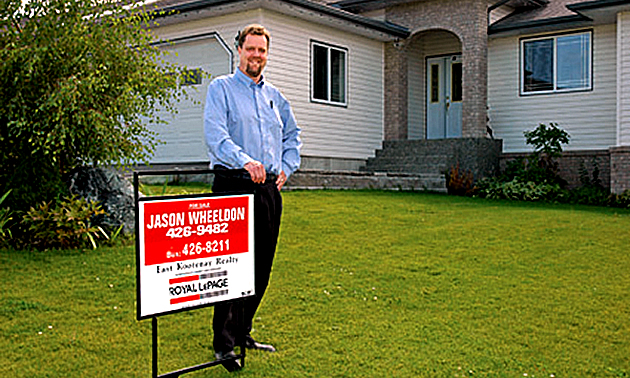 Jason Wheeldon standing next to a sold sign in front of a house. 