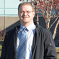 Man in business wear standing outdoors with a large building in the background, and a sign saying Western Financial Place