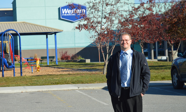 Man in business wear standing outdoors with a large building in the background, and a sign saying Western Financial Place