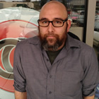 Young bald man wearing glasses and a beard stands outside a storefront window