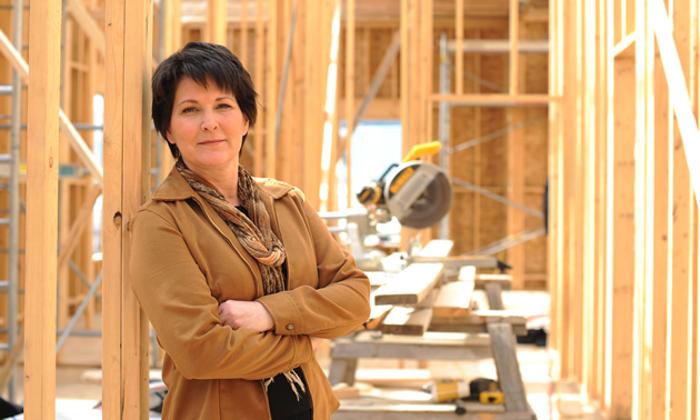 Woman stands, arms folded, inside a building under construction.