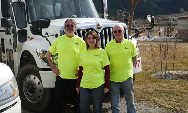 Cynthia Howard, manager of Kettle Valley Waste, stands with owner Ron Liddle and a driver. They all wear bright yellow company shirts.