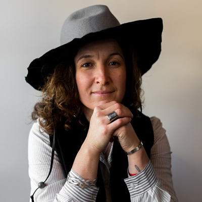 Kat Cadegan, jewelry designer, poses wearing a wide-brimmed hat
