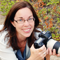 Smiling young woman holding a professional-style camera, lying prone on a pathway