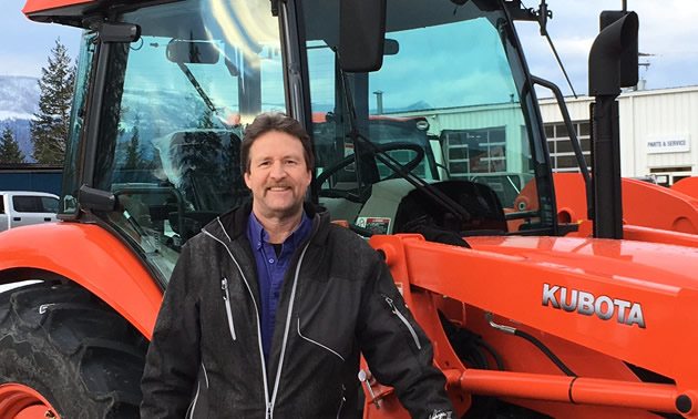 Darrell Kemle standing in front of orange tractor. 