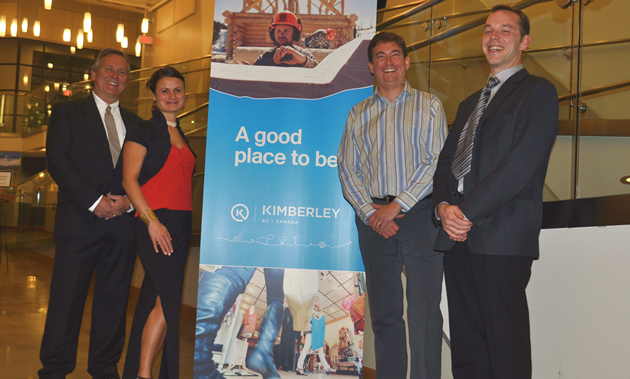 Four people in formal wear stand around a blue banner with pictures that says 