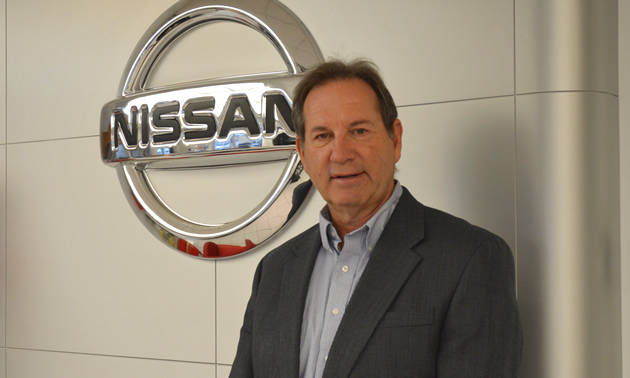 Jim Szakacs wears a suit jacket and stands in front of a large, silver Nissan symbol.