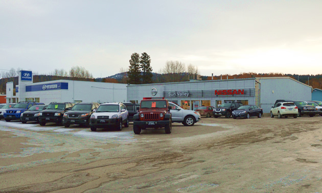 A white building has cars displayed out front.