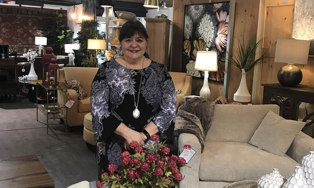 Kootenai Moon owner Valerie Semeniuk is sitting in her store with furniture and lamps in the background.