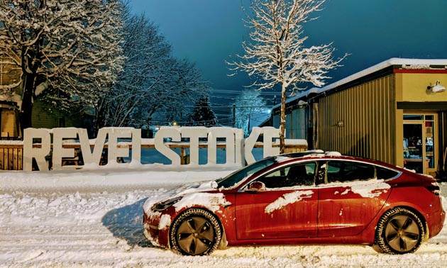 Red electric car parked in front of Revelstoke sign. 