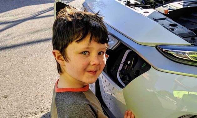 Child standing in front of electric car. 