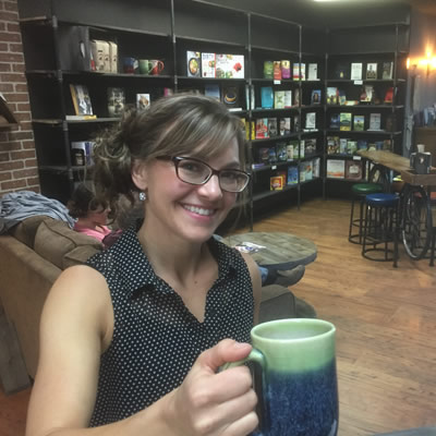 Woman holding a cup of coffee and smiling into camera. 