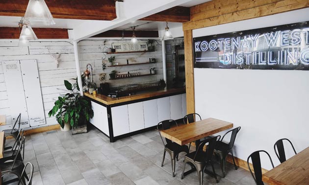 Interior of Kootenay West Distilling showing wood-topped tables and black chairs. 