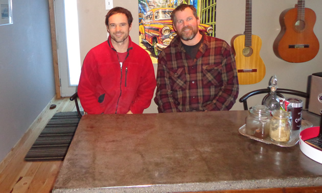 two men casually dressed seated behind a concrete countertop