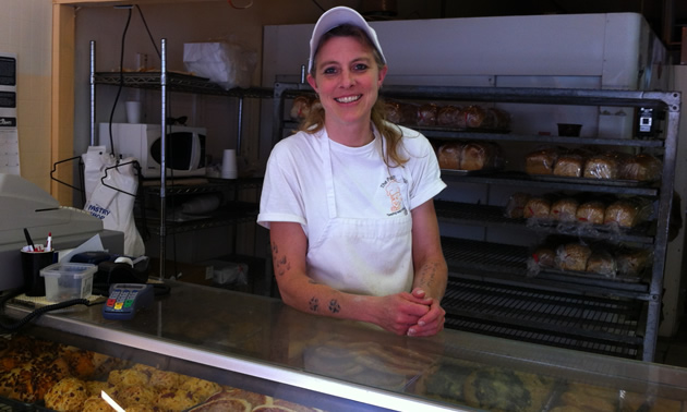 Smiling woman in white, standing behind a waist-high pastry display case
