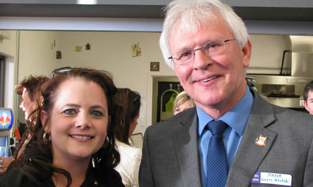 Close-up of smiling, dark-haired woman and taller, white-haired man wearing a suit and tie.