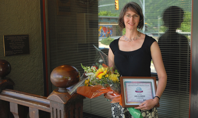 Lara Ellenwood of Ellenwood Homes stands with a bouquet and her Influential Women in Business Award certificate.
