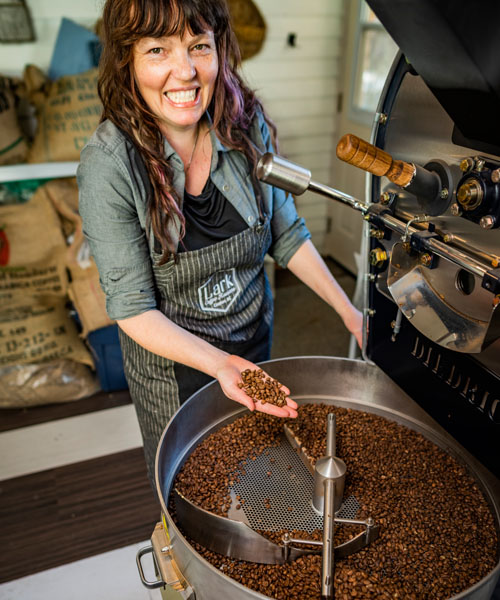 Ilana Cameron standing at coffee roaster, holding beans in palm of her hand. 