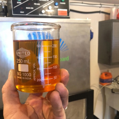 Person (unseen, just a hand in photo) holding a glass container full of biodiesel. 