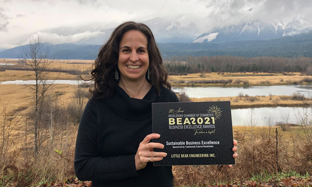 Owner of Little Bear Engineering holding Business Excellence award. Photo is taken outside in front of scenic mountains. 