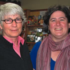 Silver-haired woman stands with younger, dark-haired woman before a wall of books on display. 