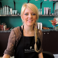 Sarah LeNeveu  stands behind the counter at Lysh Hair Salon in Fernie, B.C. Behind her is a turquoise wall and hair products. 