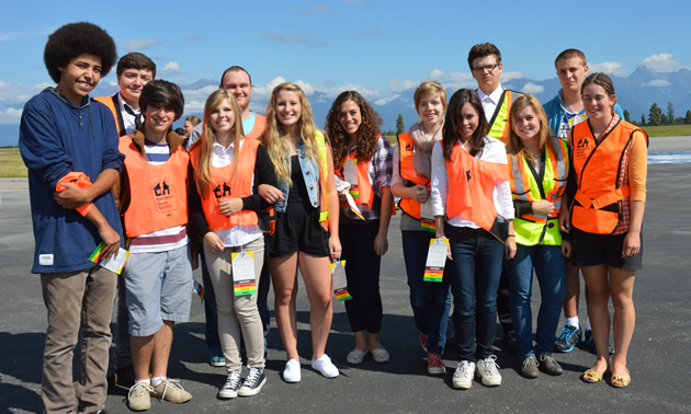A group of young people wearing orange safety vests, outdoors on a sunny day