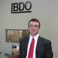 Young businessman in front of a reception desk; wall behind desk bears the logo BDO