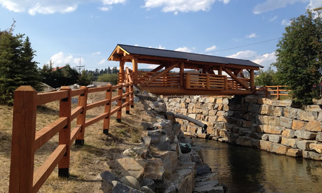 A pedestrian, timber-frame wooden bridge with a metal roof spans Mark Creek in Kimberley, B.C.