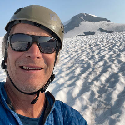 “Powder Matt” Mosteller looking into camera, snowy mountain in background. 
