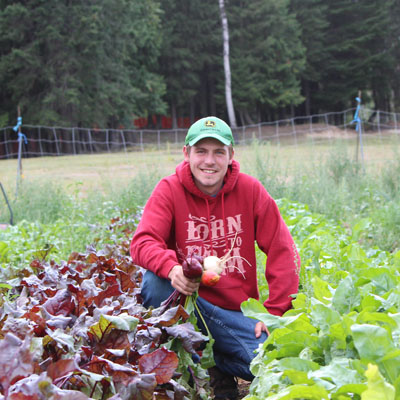 Matthew Carr crouching in field of veggies. 