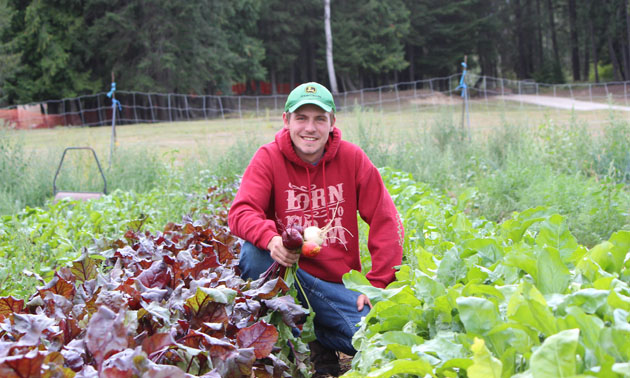 Matthew Carr crouching in field of veggies. 