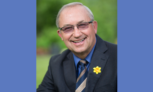 Mayor Lawrence Chernoff wears a suit with a daffodil lapel pin and glasses while smiling in the outdoors. 