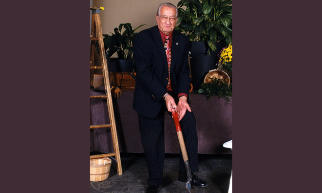 Mayor Dieter Bogs is wearing a suit and posing against gardening supplies with a shovel.