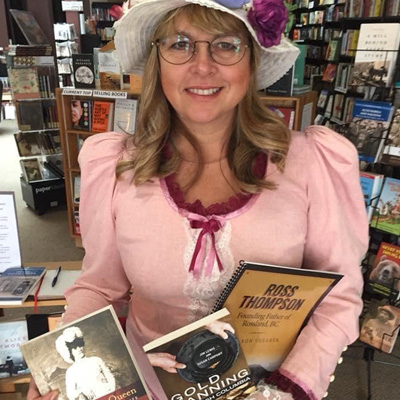 Michelle Fairbanks, dressed in pink old-fashioned dress and floppy white hat, holding a selection of books. 