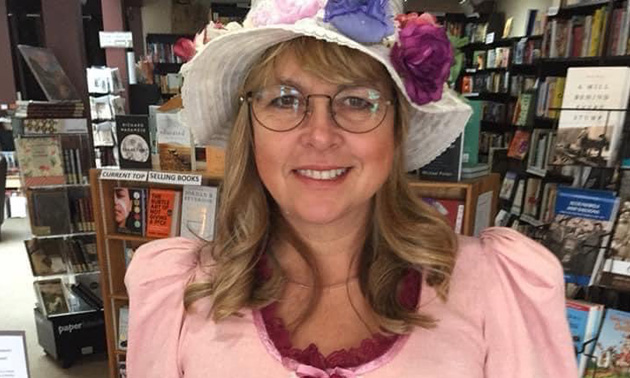 Michelle Fairbanks, dressed in pink old-fashioned dress and floppy white hat, holding a selection of books. 