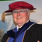 Close-up of smiling white-haired man wearing university convocation robes and hat
