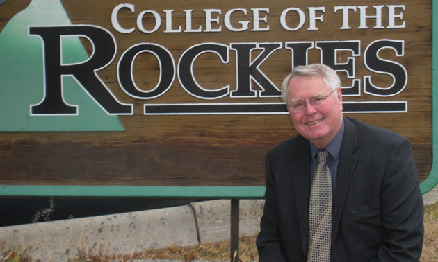 White-haired man in business suit and tie, with College of the Rockies sign immediately behind him.