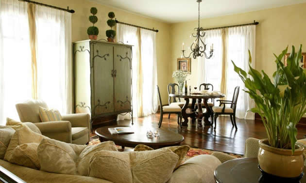 A light-filled room features a pale, antique wardrobe, ivory sofa and chair, and a dining area with dark hardwood floor and dark wood table and chairs 