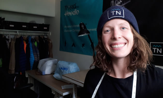 A seamstress is standing in her sewing shop with a big smile on her face.