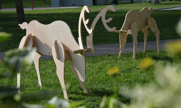 Two wooden deer appear to graze in a field, framed by blurry weeds.